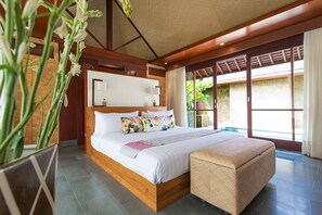Ein geräumiges Schlafzimmer mit einem großen Bett, einem Holz-Kopfteil und Blick auf einen Garten durch große Schiebetüren.