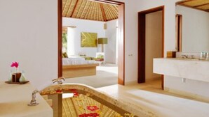A bathroom with a stone bathtub, wooden ceiling, and a visible bedroom in the background.