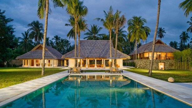 A resort with a swimming pool, thatched-roof buildings, and palm trees.