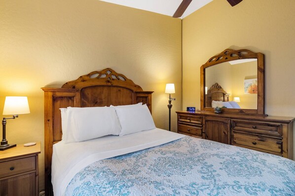 A hotel room with a wooden bed frame, a large mirror, and a bedside table with a lamp.