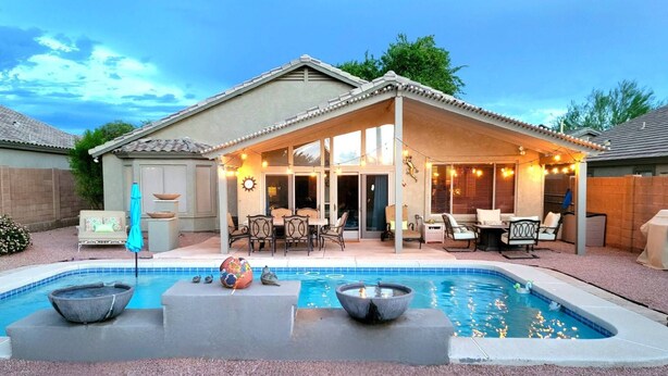 Un patio trasero con piscina, mobiliario exterior y un área de patio techada.