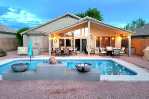 A backyard with a swimming pool, outdoor furniture, and a covered patio area.