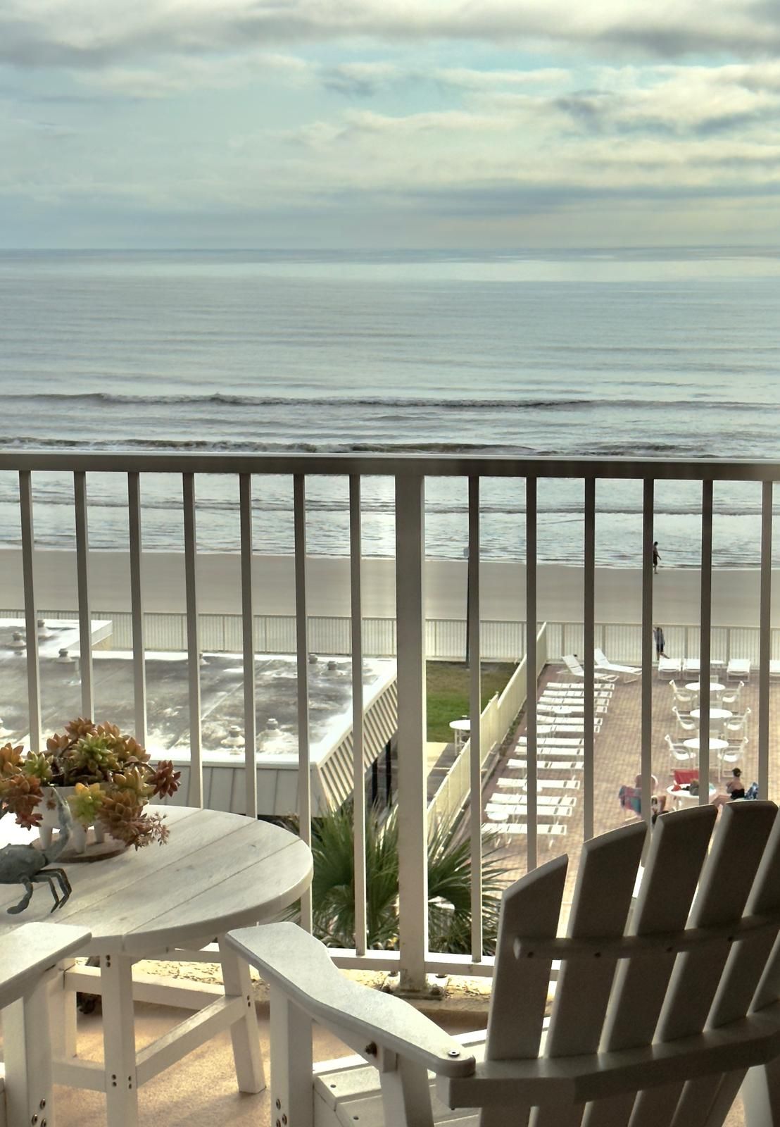 A balcony with a view of the ocean, a table with chairs, and a railing.