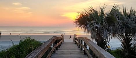A wooden boardwalk leading to a beach with a sunset in the background.