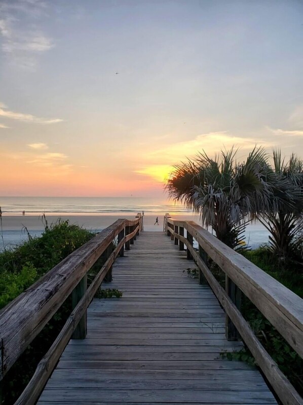 A wooden boardwalk leading to a beach with a sunset in the background.
