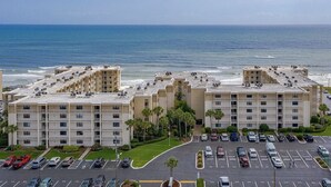 Ein Hotel direkt am Strand mit mehreren Etagen, einem Parkplatz und Blick auf den Ozean.