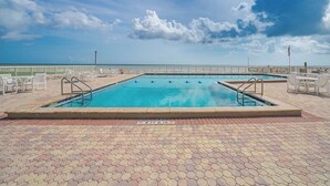Ein rechteckiger Pool mit zwei Sprungbrettern, umgeben von Fliesen in Sechseckform und weißen Liegestühlen.