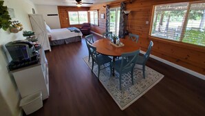 A cozy cabin with a wooden interior, a dining area with blue chairs, a bed with a white comforter, and a kitchenette with a refrigerator and a coffee maker. - Country Home at the Crossroads (Springville)
