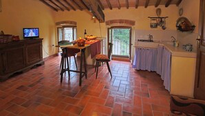 A rustic kitchen with terracotta tiles, wooden beams, and a dining area with a TV. - Farmhouse in Umbertide with Pool (Umbertide)
