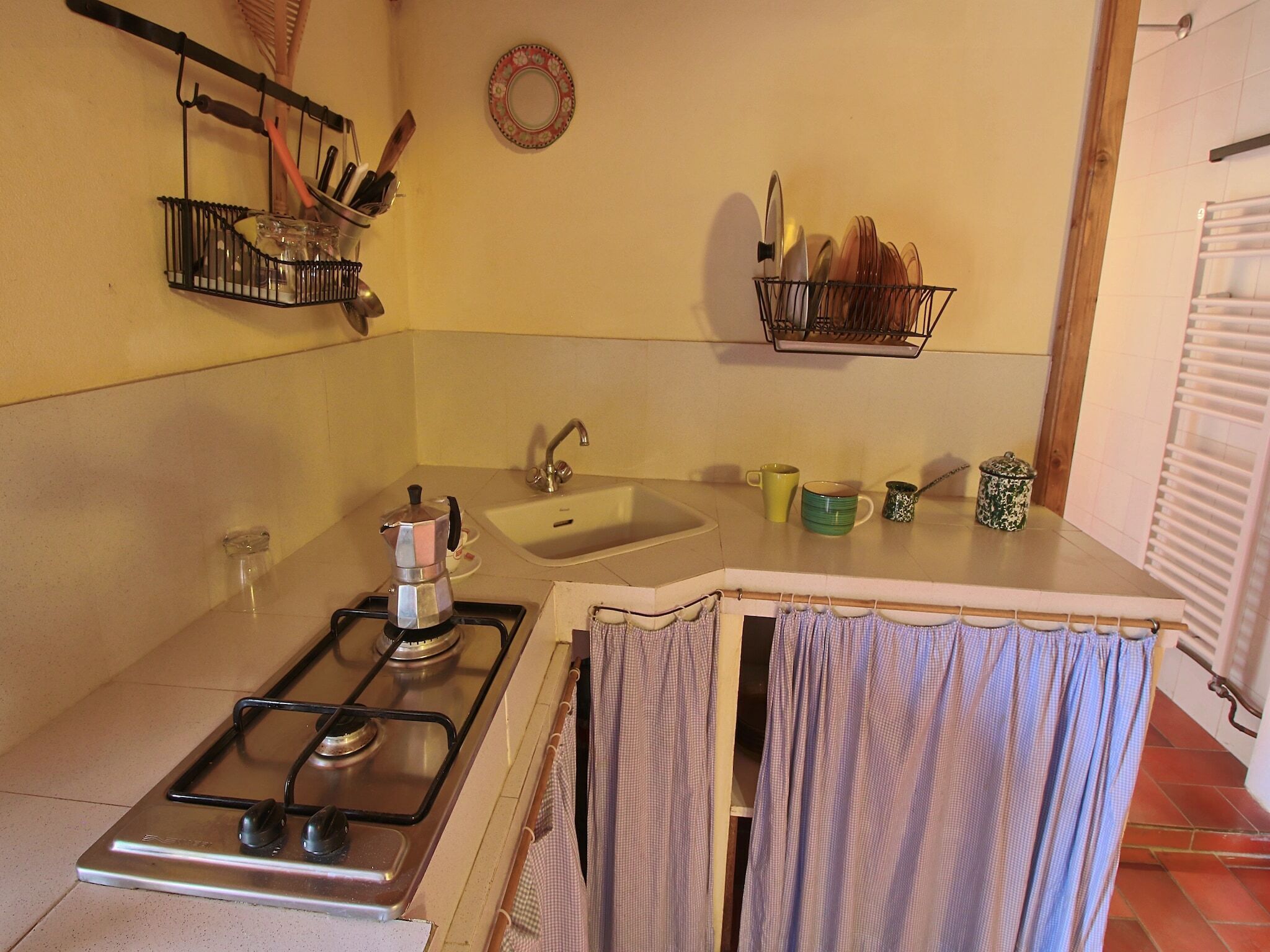 Une cuisine compacte équipée d’une cuisinière à gaz, d’un évier et de supports pour ustensiles fixés au mur.