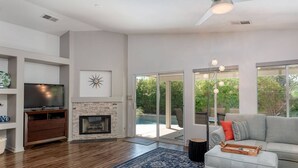 Una sala de estar moderna con chimenea, un televisor de pantalla plana y un ventanal con vista a una piscina.