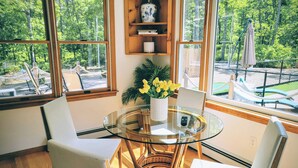 A room with a glass table and chairs, a vase with yellow flowers, and a bookshelf. - Modern Cape, Private Heated Salt Water Pool,  Minutes to Beaches/Golf/Lakes (Brewster)