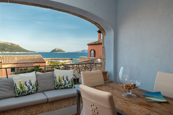 A balcony with a view of the sea, a stone wall, and a table with a glass bowl.