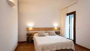 A bedroom with a bed, two bedside lamps, a wooden headboard, a nightstand, and a window with curtains.