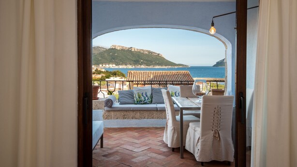 An open doorway to a balcony with a view of the sea and a mountainous landscape.