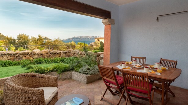 Une terrasse extérieure avec une table dressée pour le petit-déjeuner, des murs en pierre et une vue sur la mer.