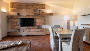 Un salon moderne avec un meuble mural en bois, un téléviseur à écran plat, une table à manger avec des chaises et un coin cuisine avec une lampe.