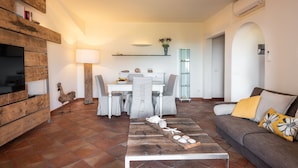 Un salon moderne comprenant un coin repas, un meuble TV en bois, une lampe sur pied et un canapé agrémenté d’un coussin décoratif.