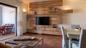 Un salon moderne avec un meuble mural en bois, un téléviseur à écran plat et un coin repas comprenant une table et des chaises blanches.