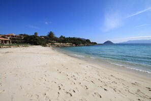 A sandy beach with footprints, a clear blue sky, and a distant mountain.