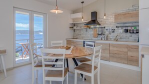 A modern kitchen with white cabinets, a wooden dining table, and a view of the sea through large windows. - Two bedroom apartment with wonderful sea view (Mimice)