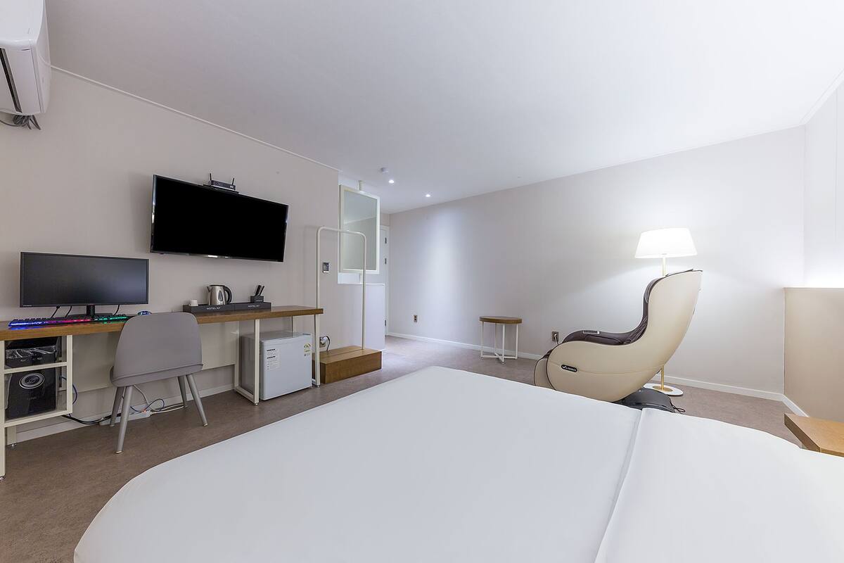 A hotel room with a bed, a desk with a computer, a chair, a TV, and a lamp.