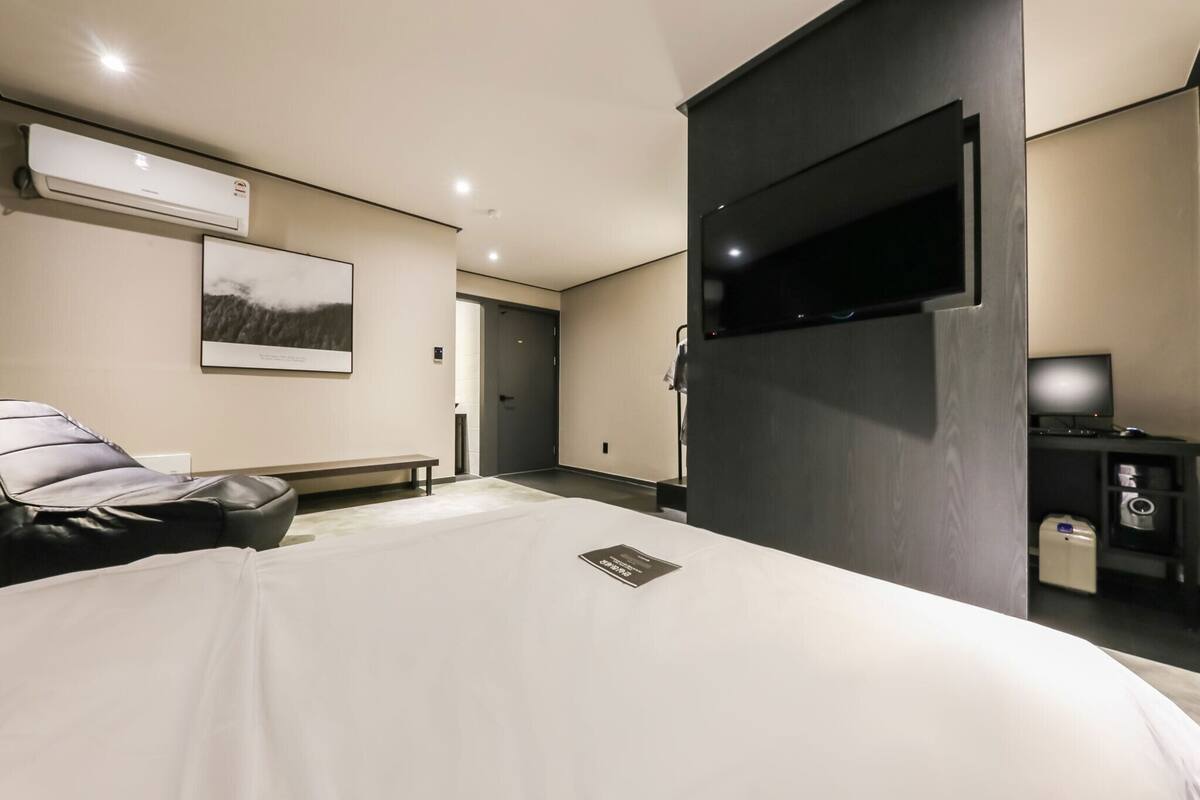A modern hotel room with a large bed, a flat-screen TV, a mounted air conditioner, and a framed picture on the wall.