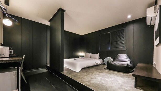 A modern bedroom with a bed, bedside table, chair, and a small desk area with a lamp. - Hotel N7 Daejeon Bus Terminal (Daejeon)