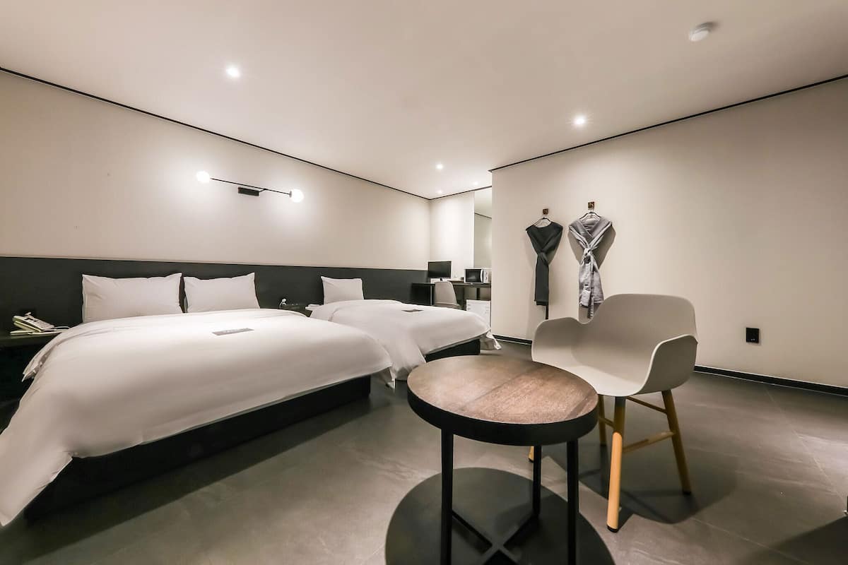 A modern hotel room with two beds, a round table, and a chair.