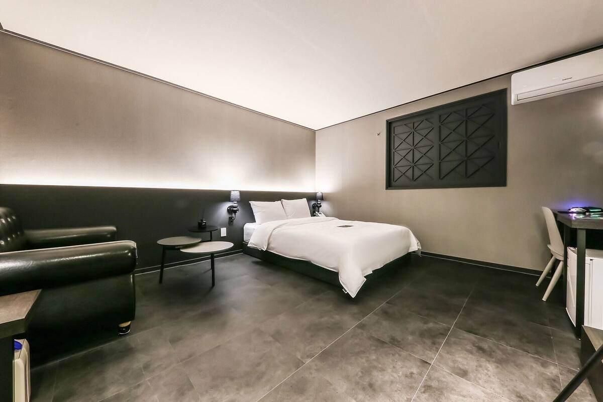 A modern hotel room with a bed, a desk, a chair, and a small table.