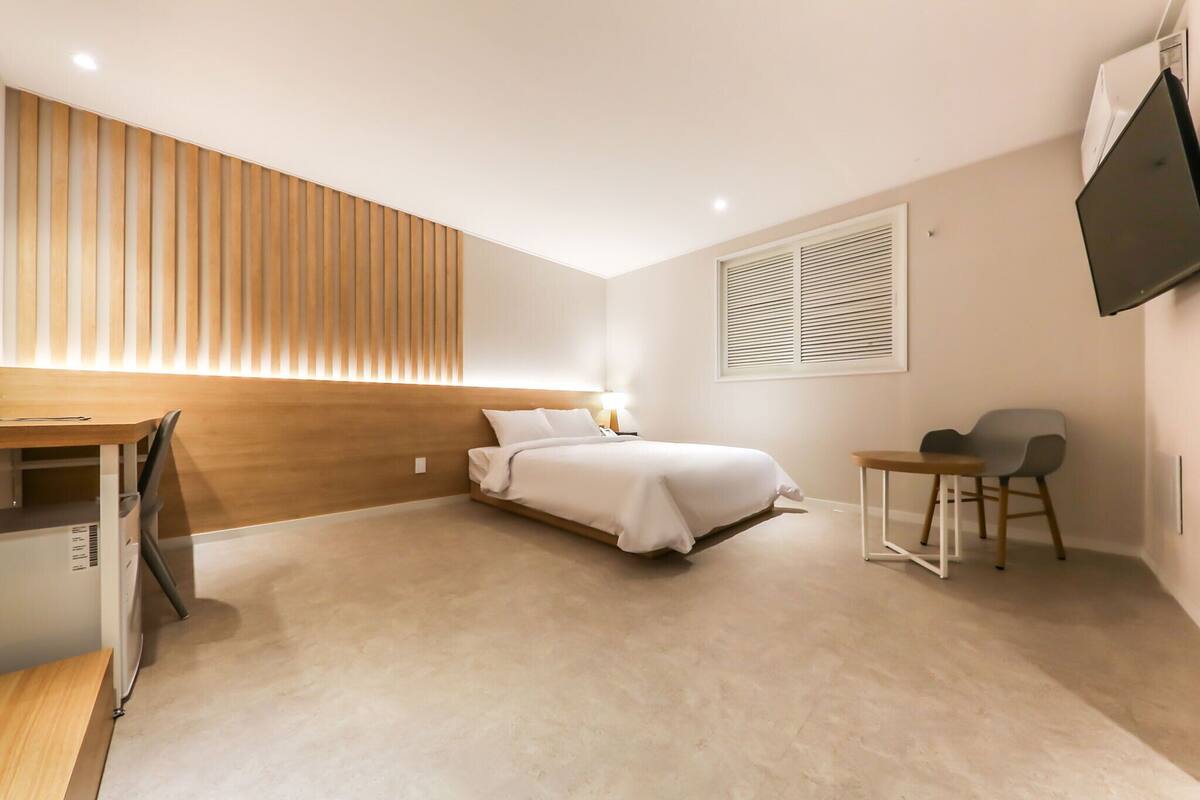 A bedroom with a bed, bedside table, chair, desk, and a TV mounted on the wall.