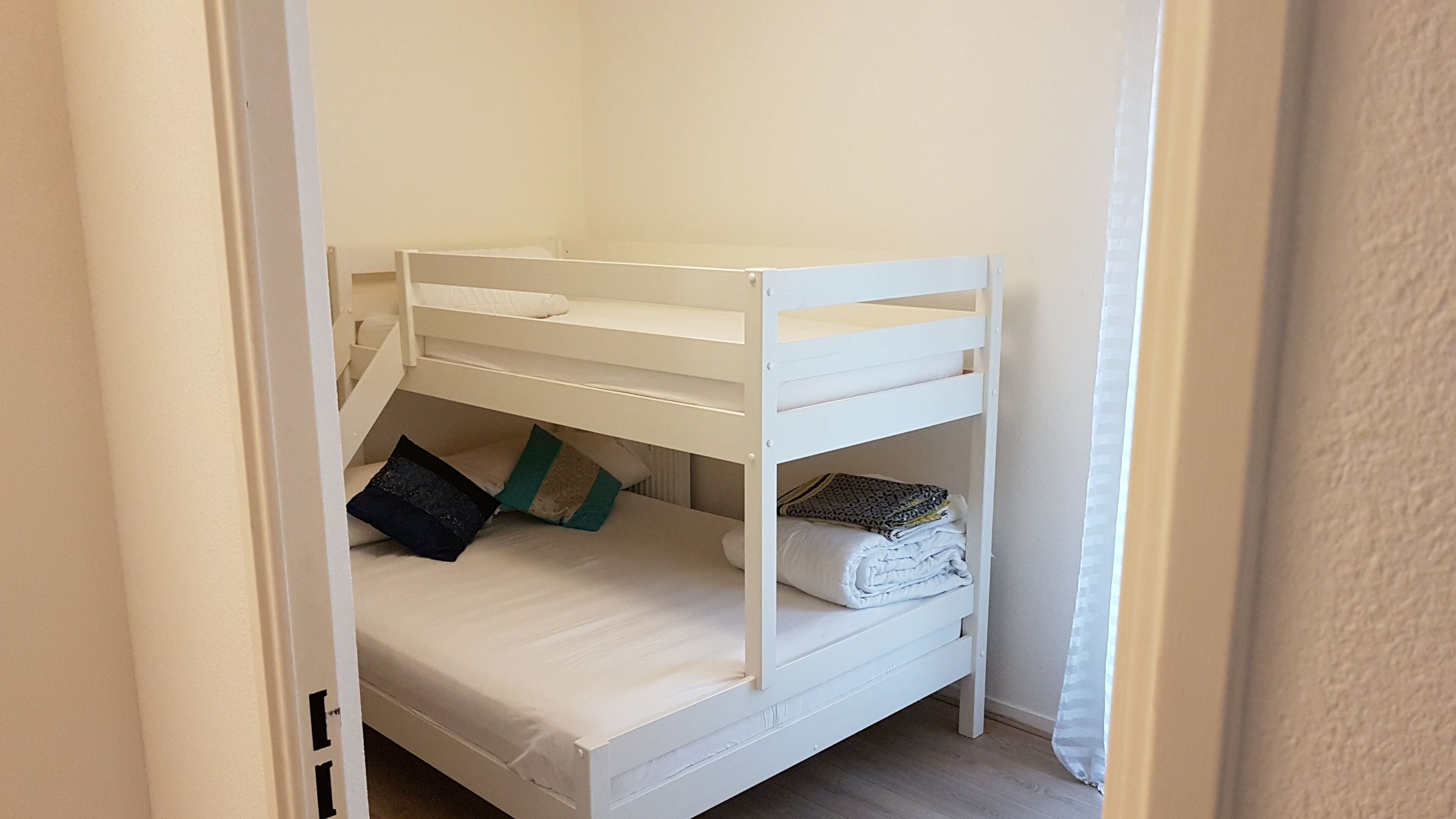A bunk bed room with a white color scheme, a door frame, and a curtain.