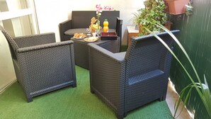 A small outdoor seating area with wicker furniture and a table set with food and drinks.