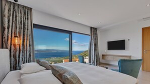 Une chambre avec un grand lit, un téléviseur fixé au mur et une vue sur la mer.