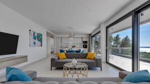 Un salon moderne avec un canapé gris, une table basse en verre et un téléviseur posé sur une étagère en bois.