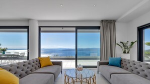 Un salon moderne avec deux canapés gris, une table basse en verre et une vue sur la mer.