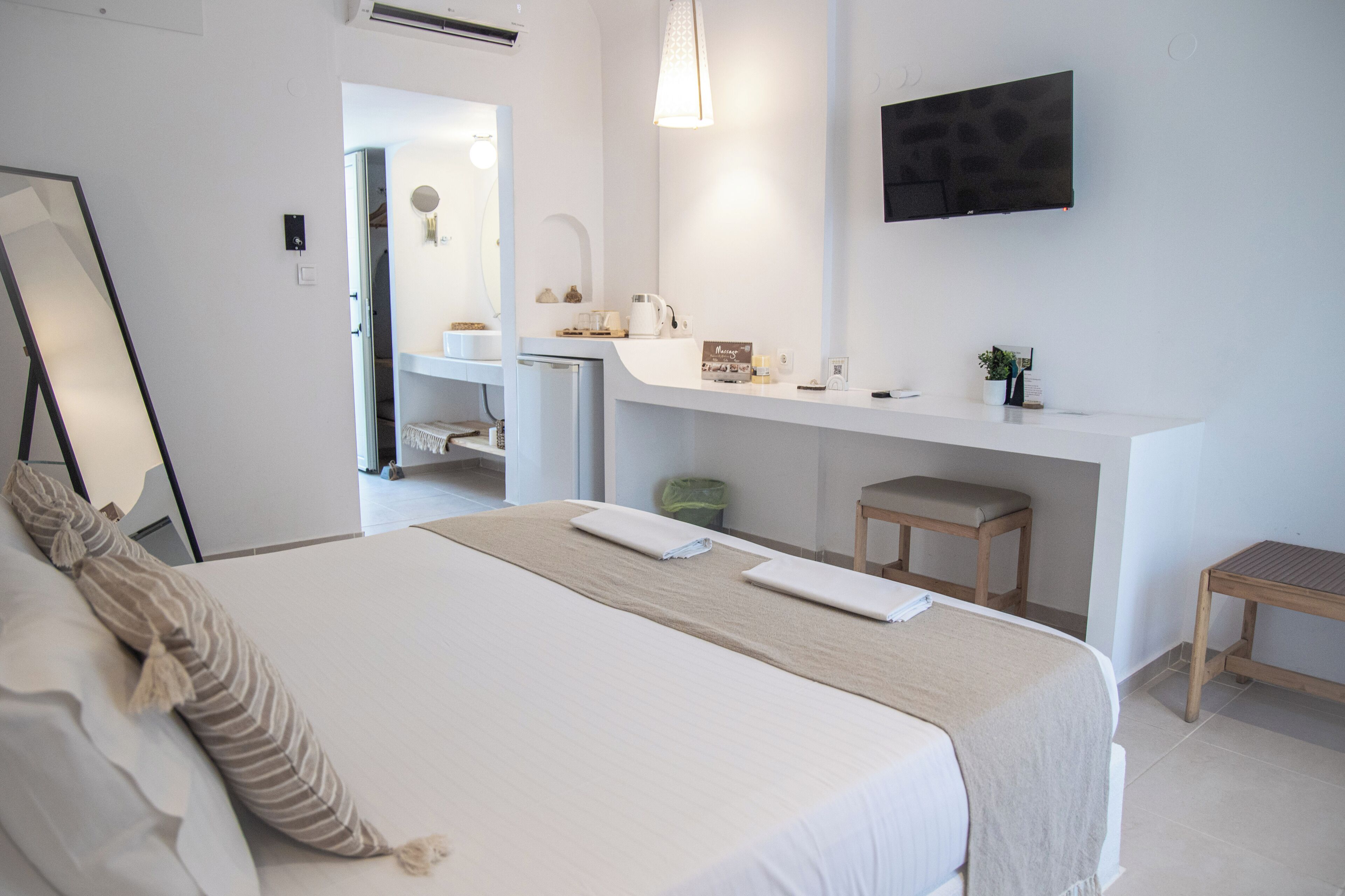 A hotel room with a bed, a desk, a mirror, a TV, and a small stool.
