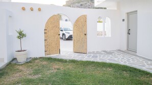 Um edifício branco com entrada pavimentada, duas portas de madeira, um vaso de planta e um carro estacionado na frente.