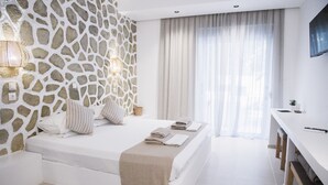 Quarto com parede de pedra, cama com almofadas, mesa de cabeceira e escrivaninha com cadeira.
