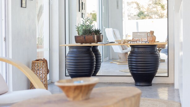 Um interior moderno com uma mesa de madeira, dois grandes vasos pretos, uma cesta de vime e uma cadeira branca.