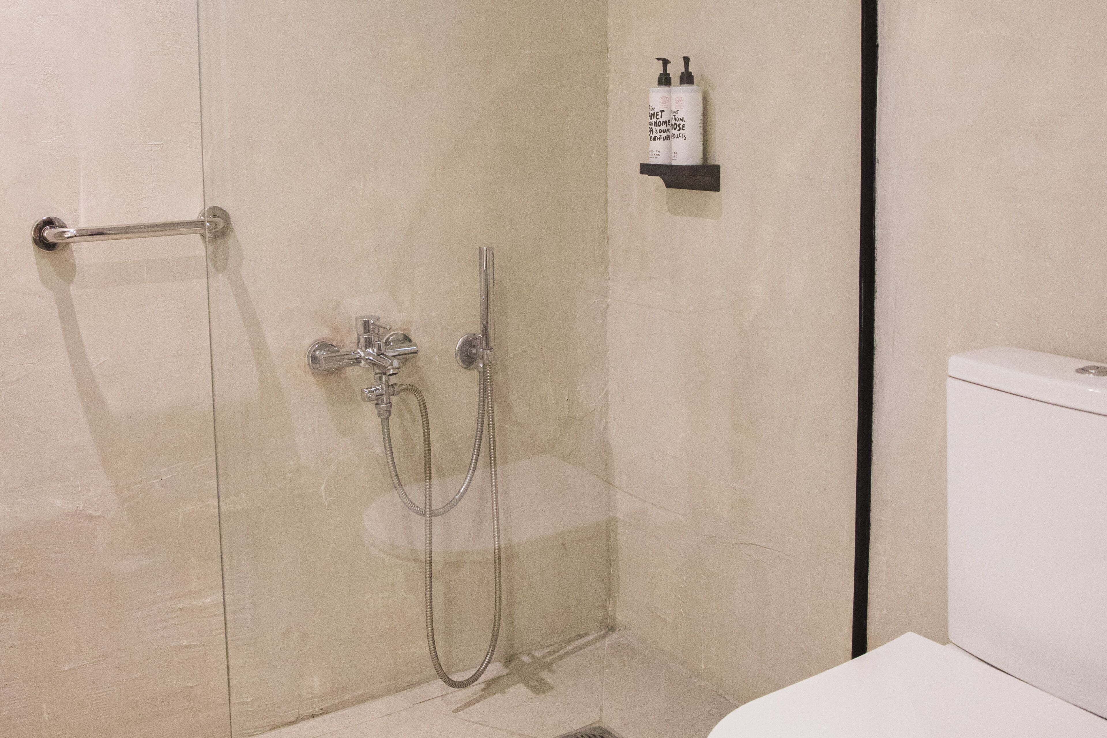 A bathroom with a glass-enclosed shower, a toilet, and a shelf with toiletries.