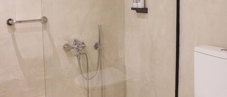 A bathroom with a glass-enclosed shower, a toilet, and a shelf with toiletries.