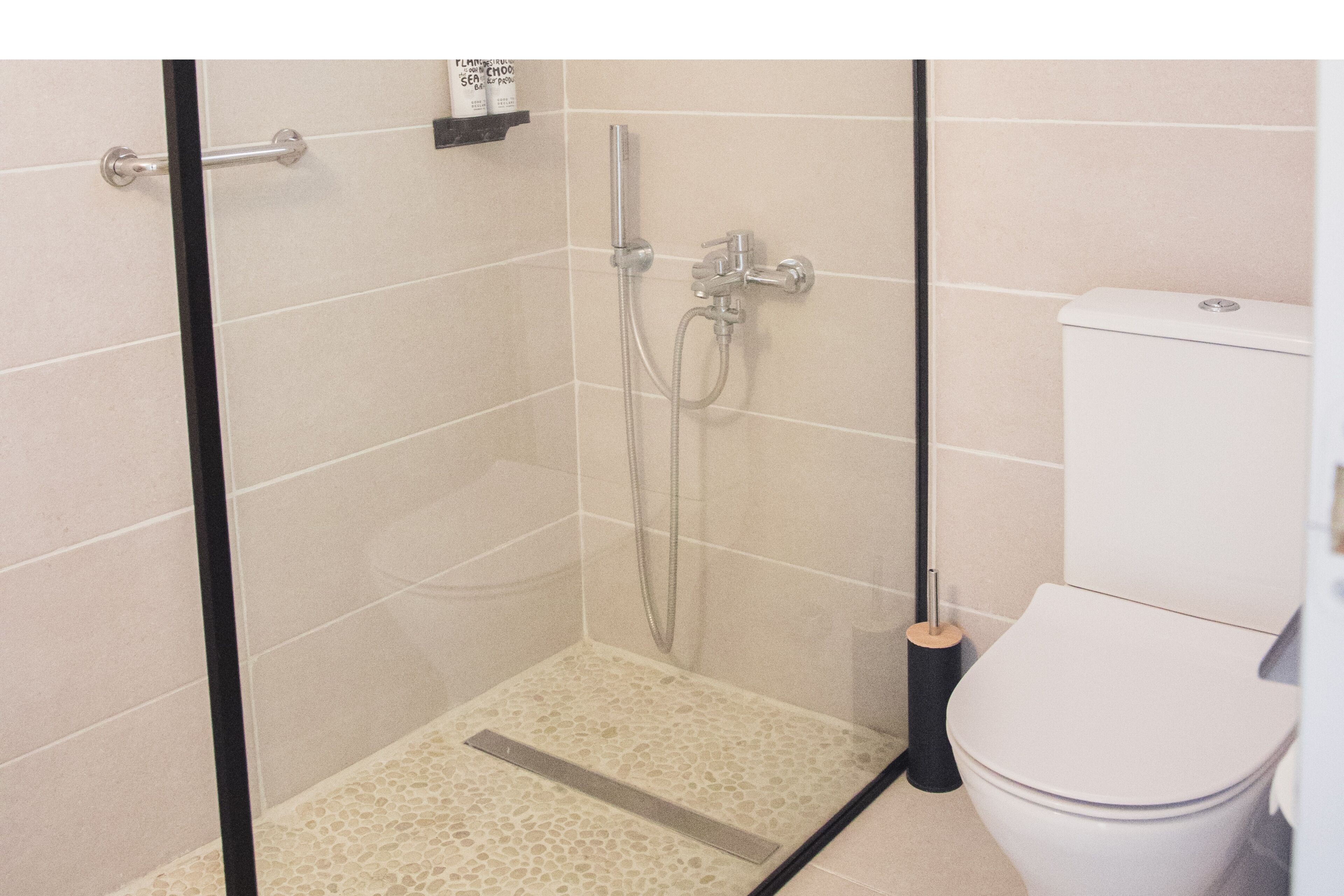 Una ducha con puerta de cristal, un inodoro y suelo de baldosas.