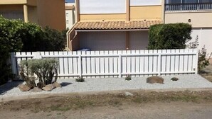 Un immeuble résidentiel avec un portail de garage fermé, une clôture blanche en bois et une allée gravillonnée.