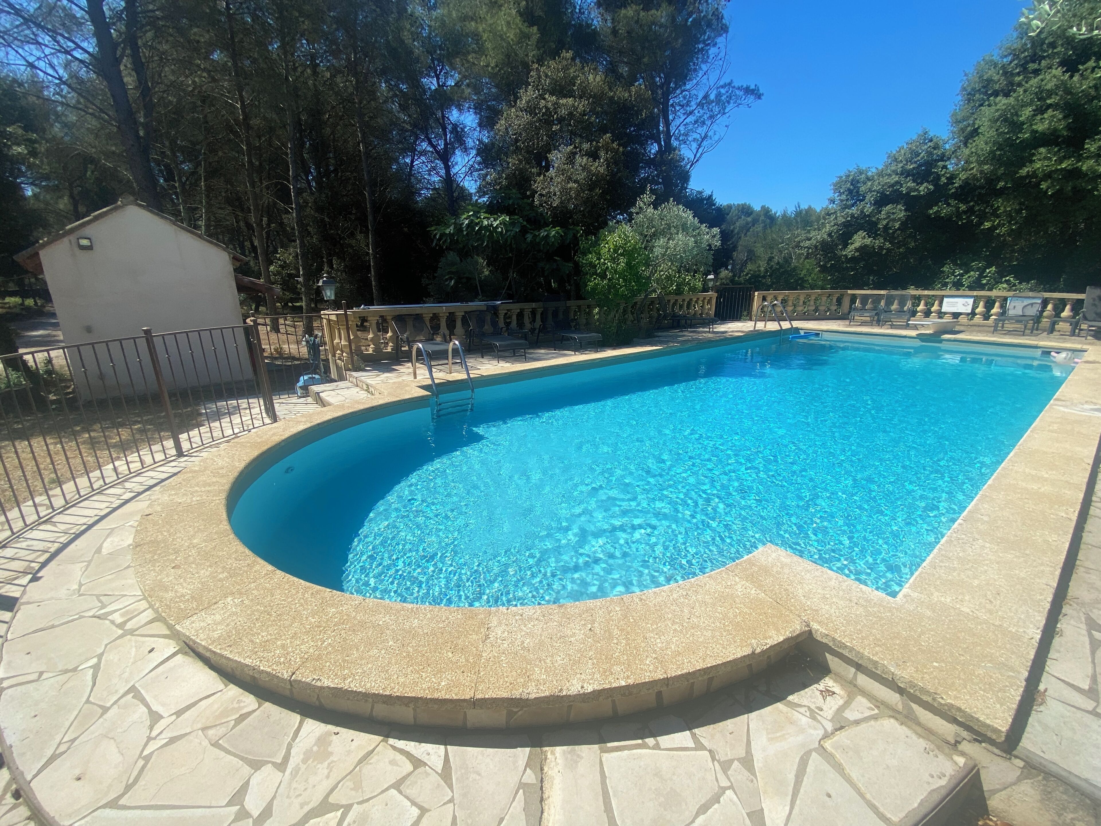 Une piscine rectangulaire à bord incurvé, entourée d’une terrasse en pierre et d’une clôture en métal.