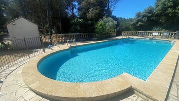 Une piscine rectangulaire à bord incurvé, entourée d’une terrasse en pierre et d’une clôture en métal.