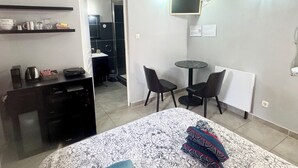 Une chambre d’hôtel avec un lit, un bureau, une chaise, une petite table et un téléviseur fixé au mur.