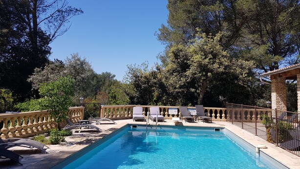 Une piscine rectangulaire à l’eau d’un bleu limpide, entourée d’une terrasse en pierre et d’une clôture en bois. On y trouve des chaises longues et une petite table près de la piscine.