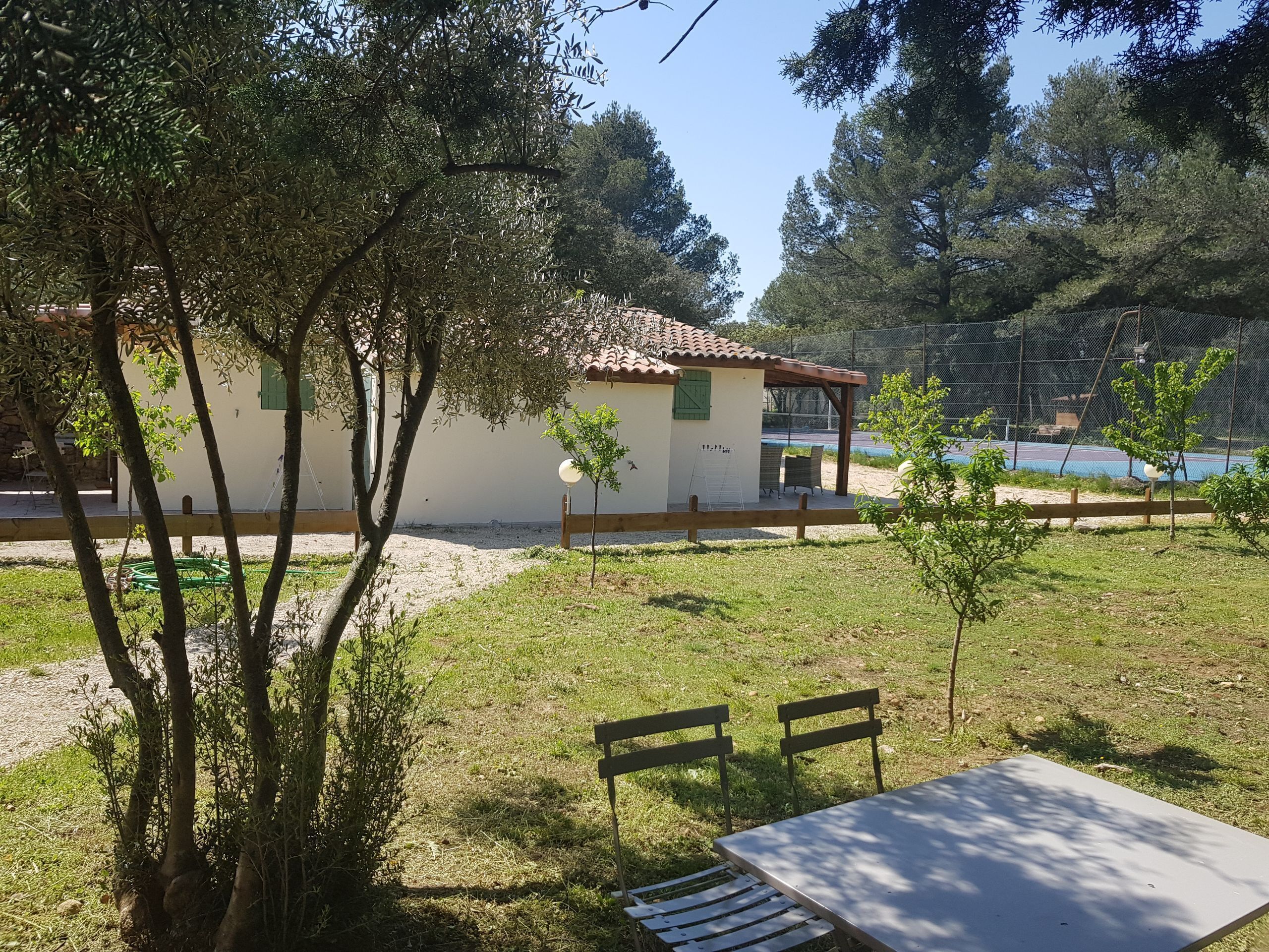 Une petite maison avec un toit en tuiles, une cour clôturée et une table avec des bancs.