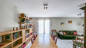 A spacious living area with a wooden dining table, chairs, a green sofa, and a bookshelf filled with books and decorative items. - Charming 3-Bedroom House Near Beach with Garden and Terrace (Les Sables-d'Olonne)